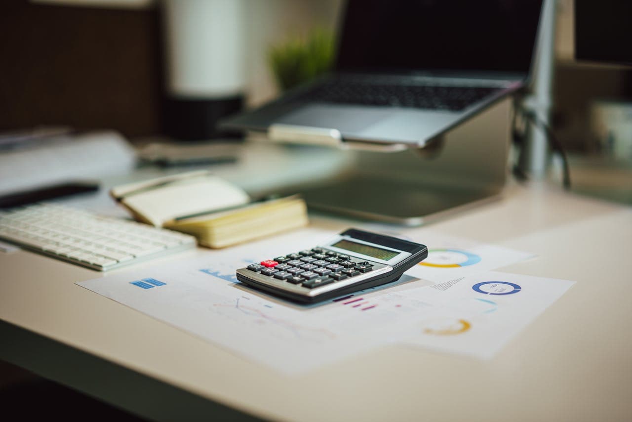 Calculator on a desk with financial charts, keyboard, and laptop in an office workspace